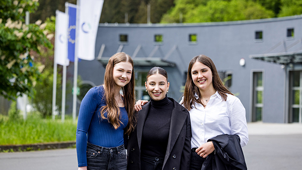 Drei junge Frauen stehen lächelnd vor dem Firmengebäude von CC Pharma und schauen in die Kamera.